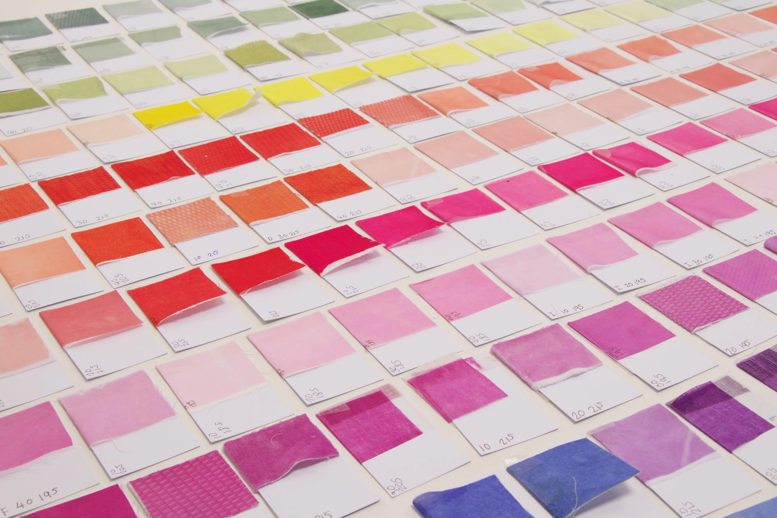 Color swatches arranged in rows, showcasing various shades from greens to pinks and blues, with some swatches torn or folded.