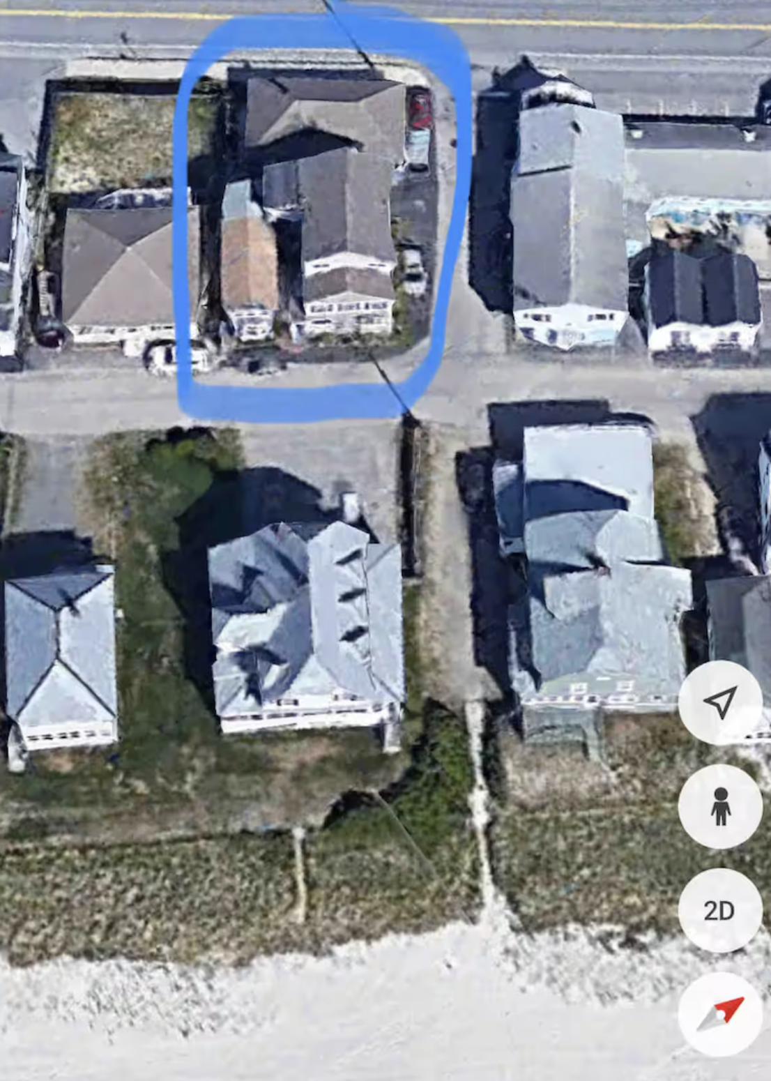 An aerial view of a neighborhood with multiple houses. One house is marked with a blue outline. The houses have gray roofs, and some have visible driveways and cars parked outside.