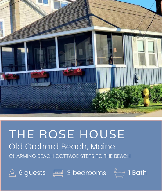 A blue house with a screened-in porch, flower boxes, and a gabled roof, located in Old Orchard Beach, Maine, with a sign advertising it as The Rose House, a charming beach cottage with three bedrooms and one bathroom.