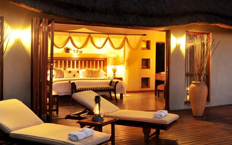 Outdoor balcony overlooking a cozy bedroom with a bed, lamps, and decorative curtains inside.