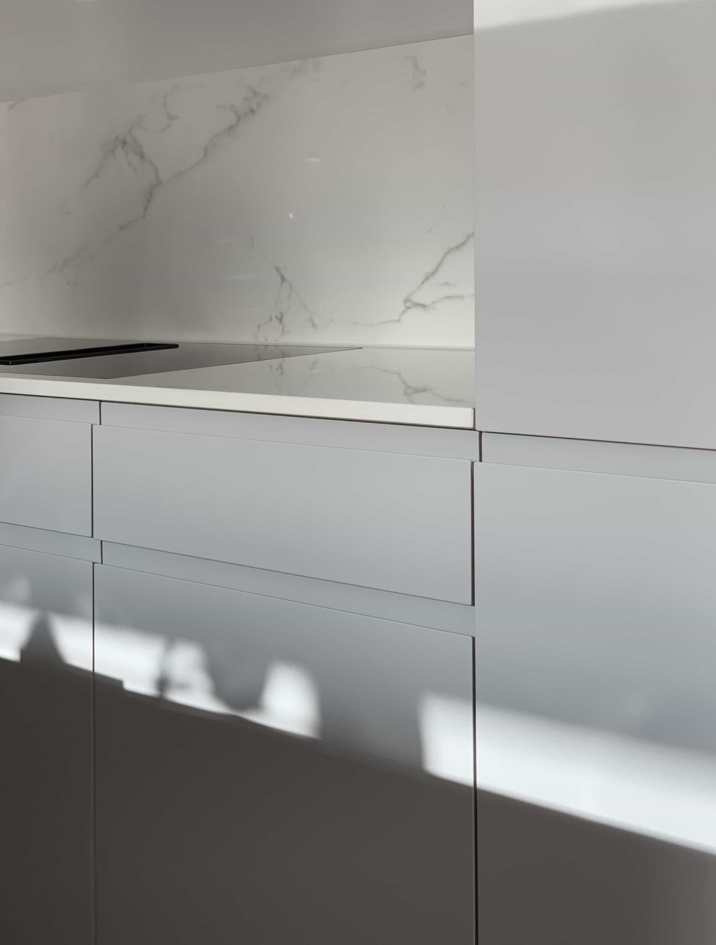 Moderne graue Küchenfronten mit Eingriffleisten und Marmorarbeitsplatte mit Rückwand.