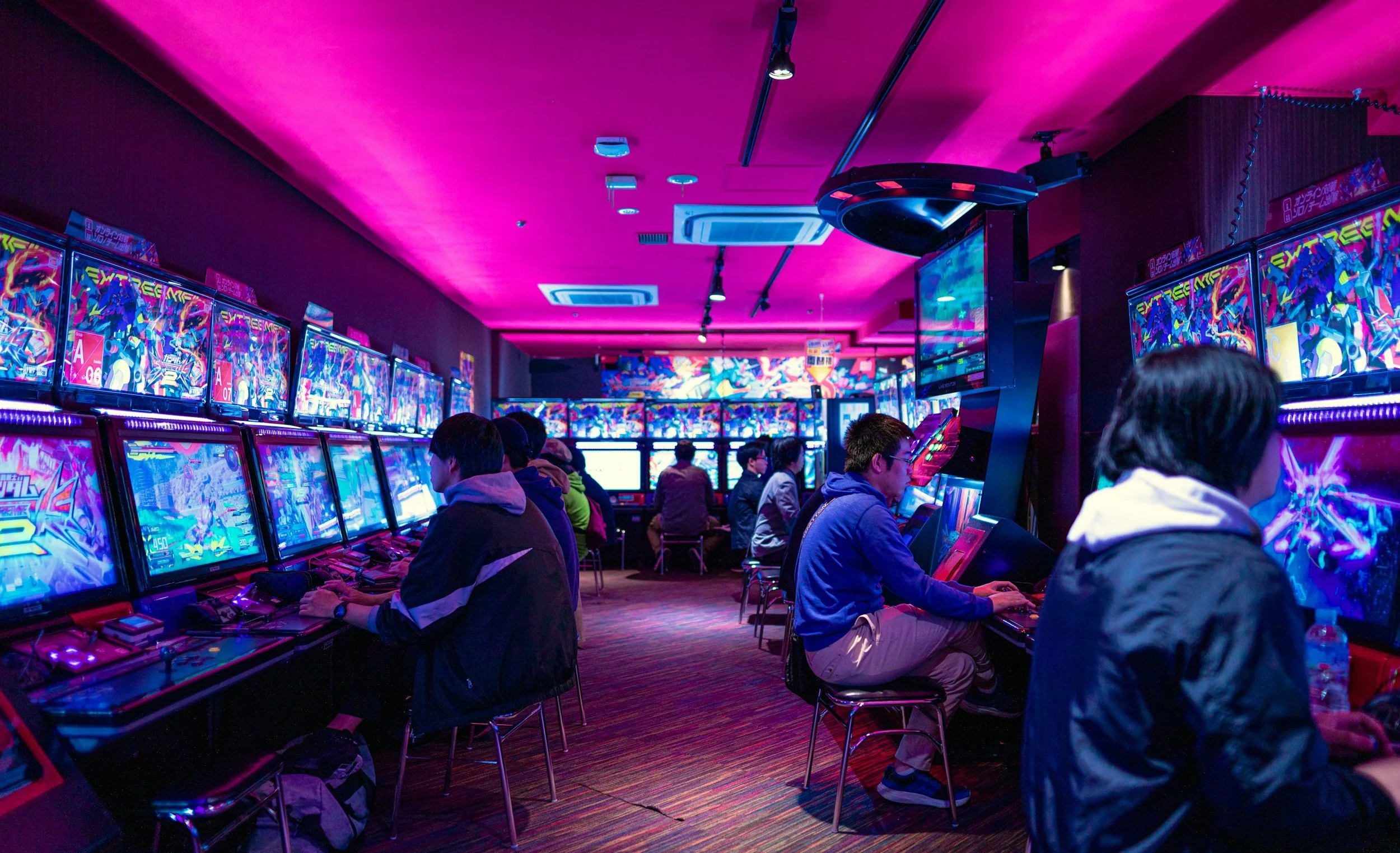 People playing arcade video games in a neon-lit arcade room.