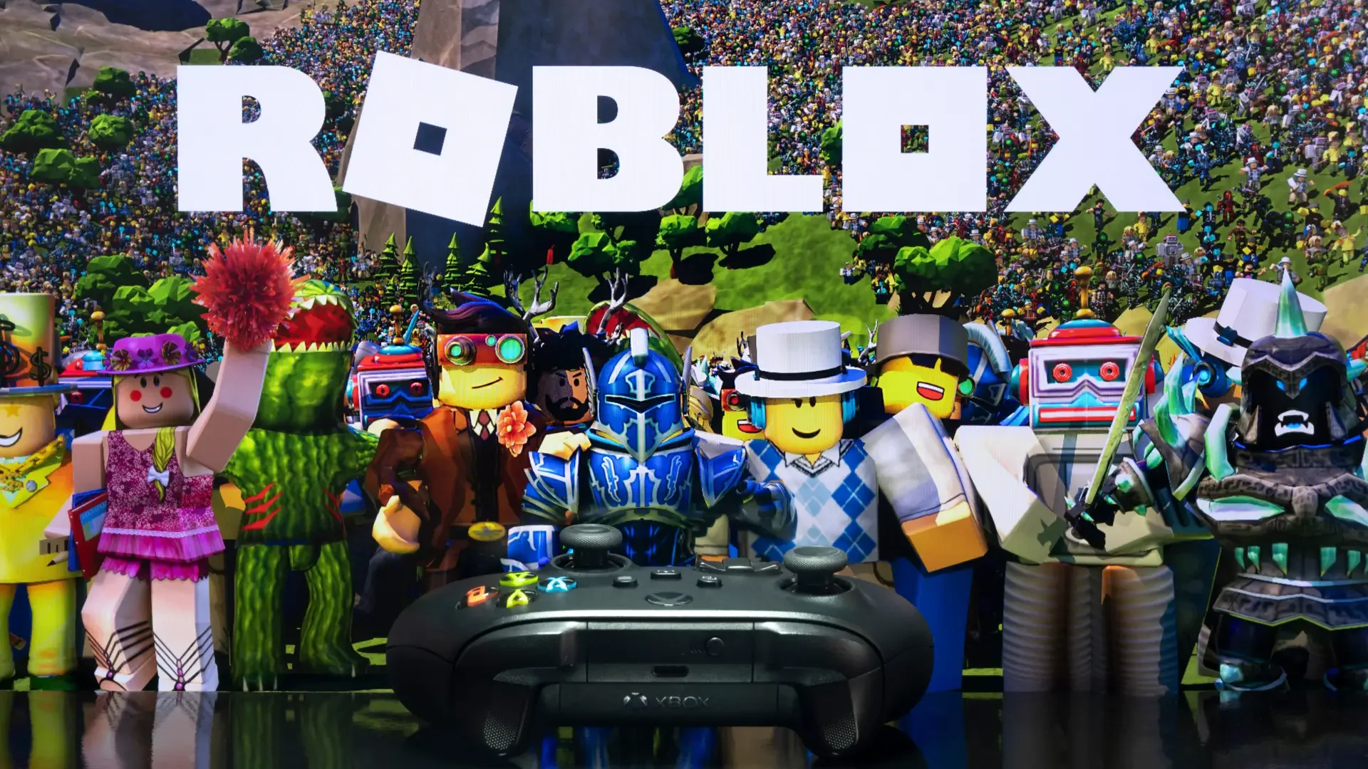 Roblox logo with a group of diverse Roblox characters in front of a colorful background of tiny Roblox figures and scenery, with an Xbox controller at the bottom.