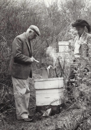 Two men outdoors, with beekeeping equipment, handling a hive or beekeeping setup