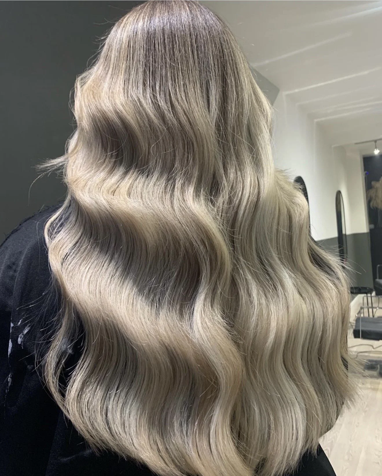 Close-up view of long, wavy, blonde hair with darker roots in a salon.
