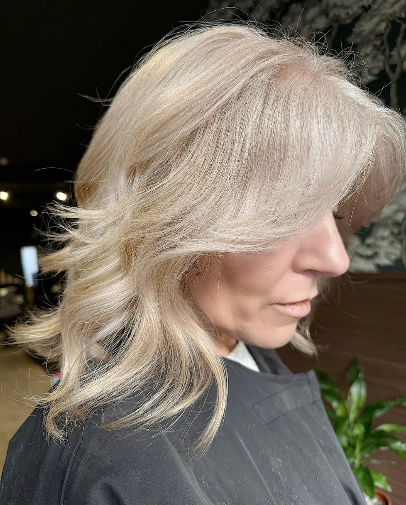 Side profile of a woman with platinum blonde wavy hair and fair skin, wearing a black salon cape.