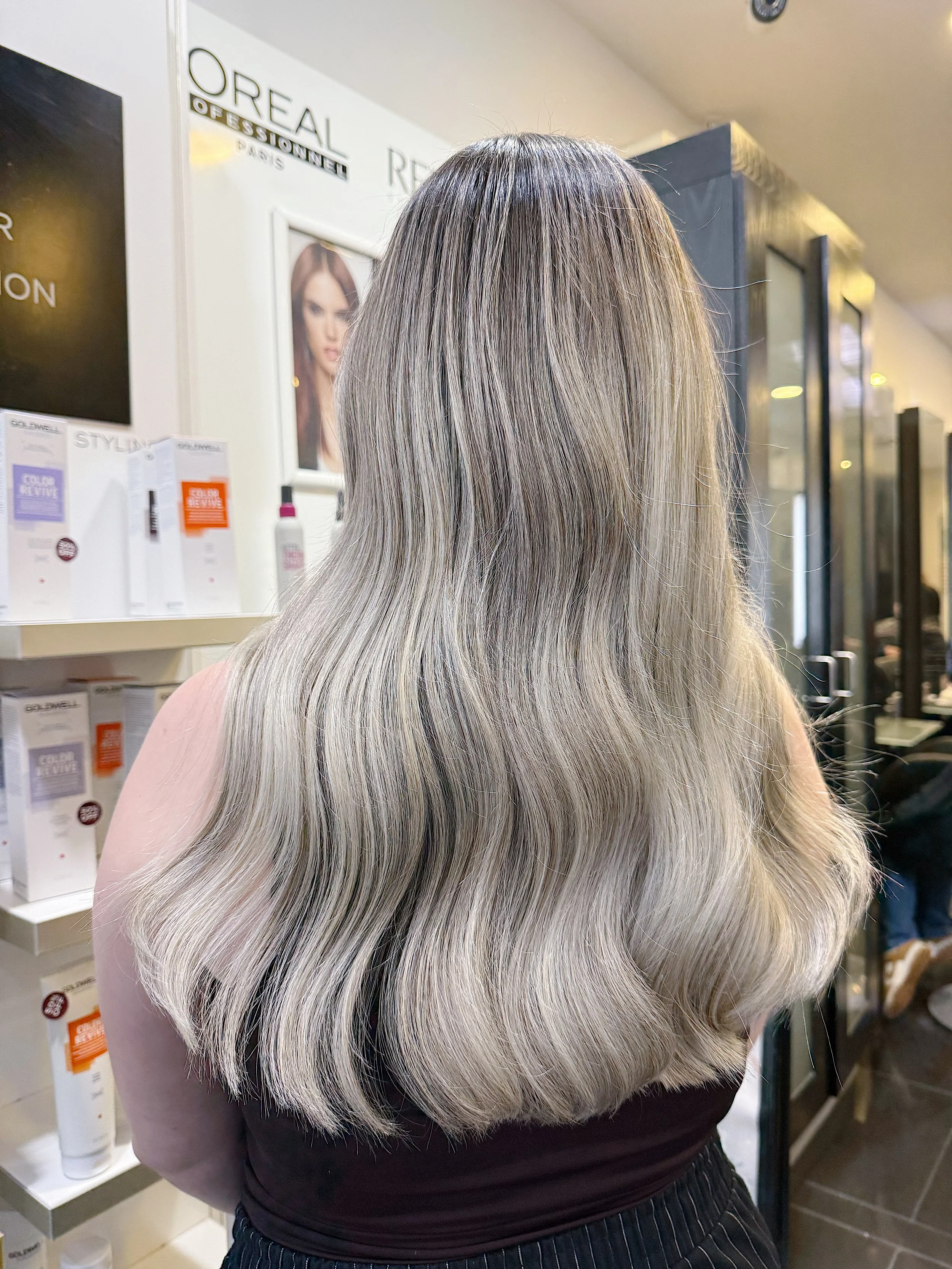 Back view of a woman with long, wavy, blonde hair in a salon.