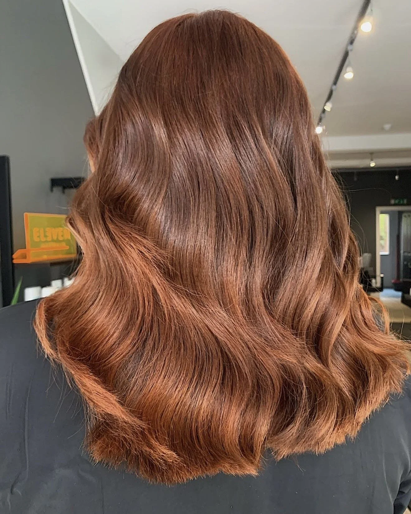 Close-up of a person's shiny, wavy, copper-red hair styled in loose waves