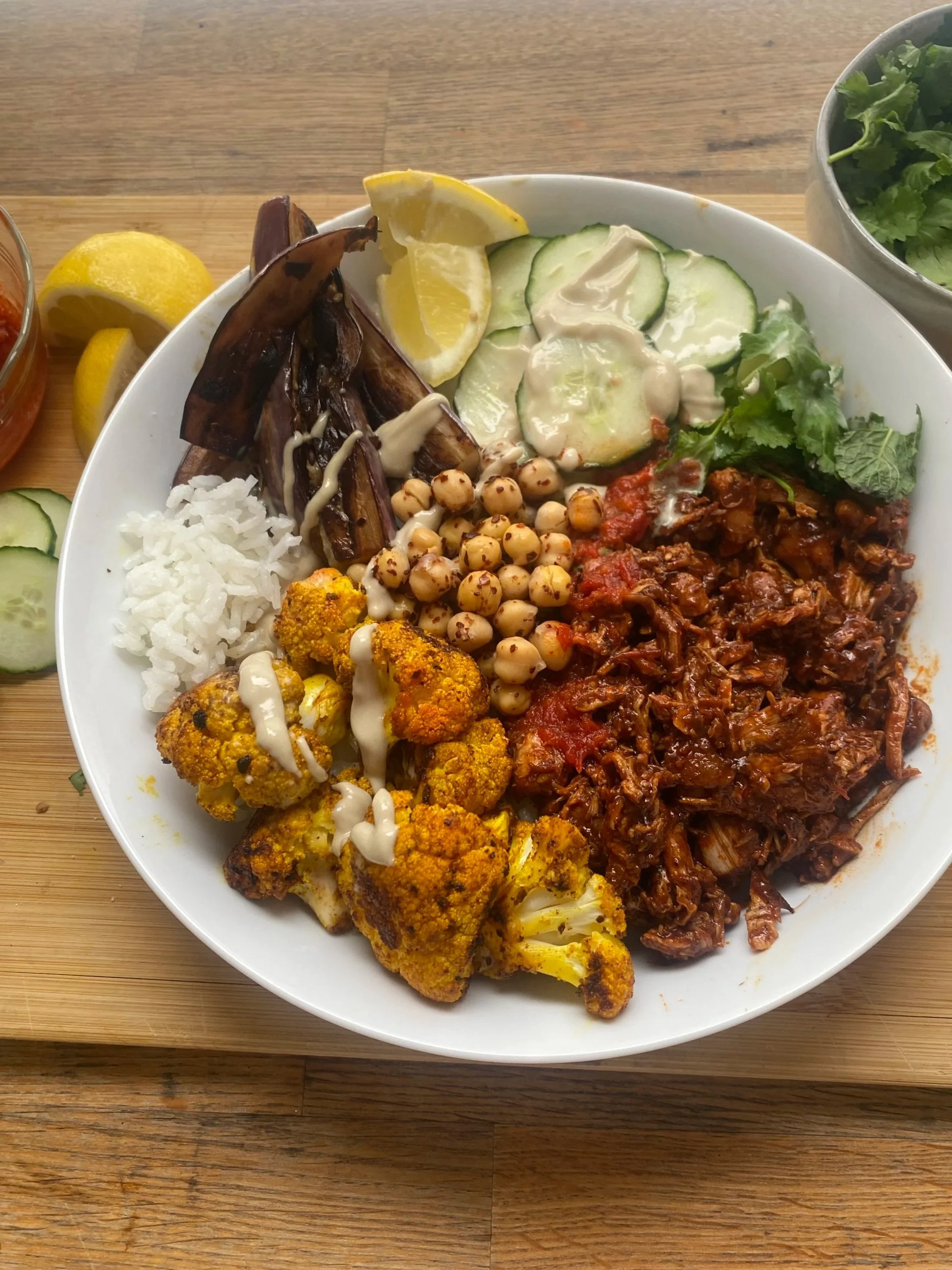 Plate with grilled eggplant, lemon wedges, cucumber slices, cucumbers with sauce, lettuce, chickpeas, cauliflower, rice, and shredded beef brisket in sauce.