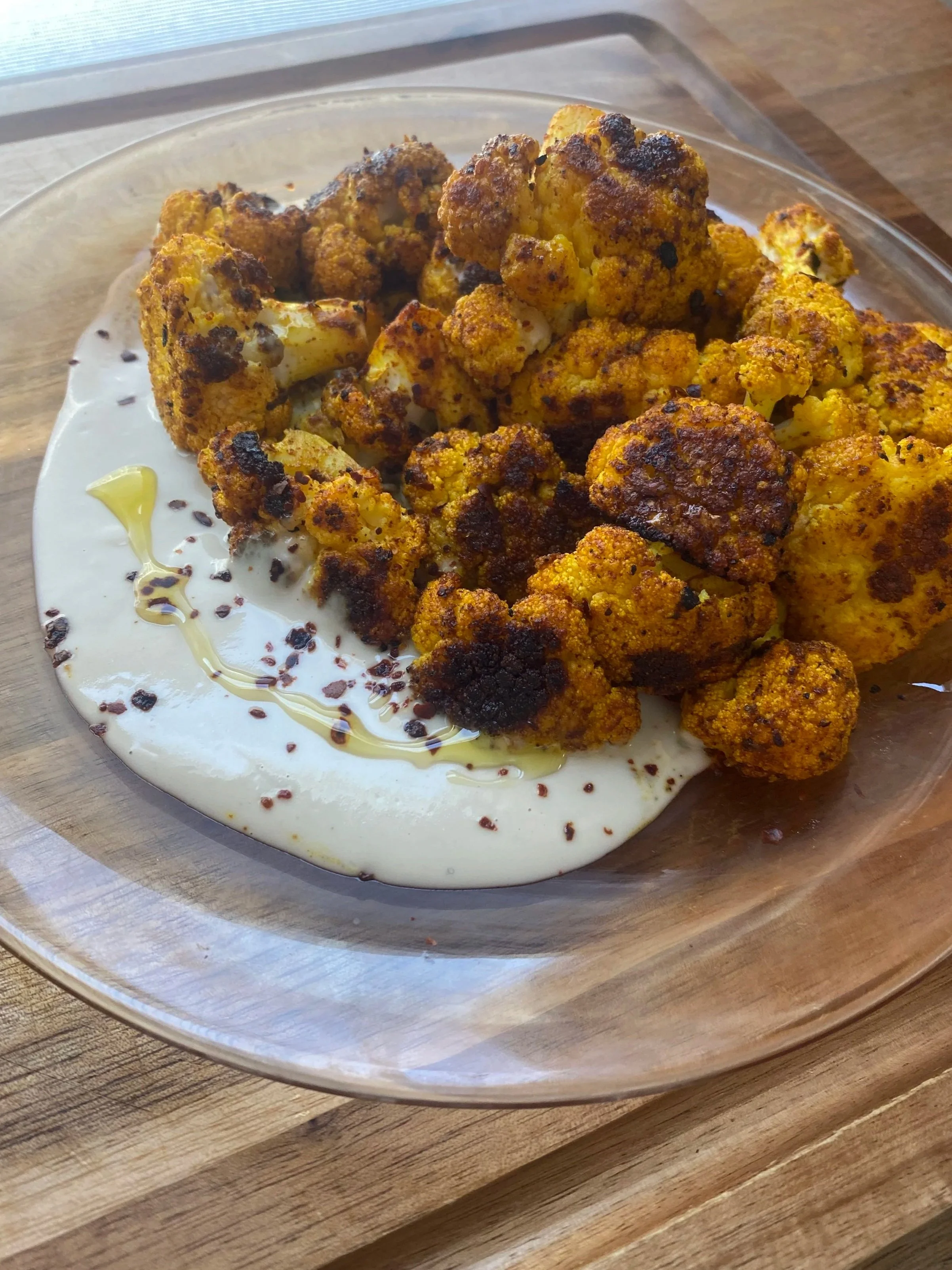 Roasted cauliflower florets served on a bed of creamy white sauce with olive oil drizzle and spices in a glass dish.
