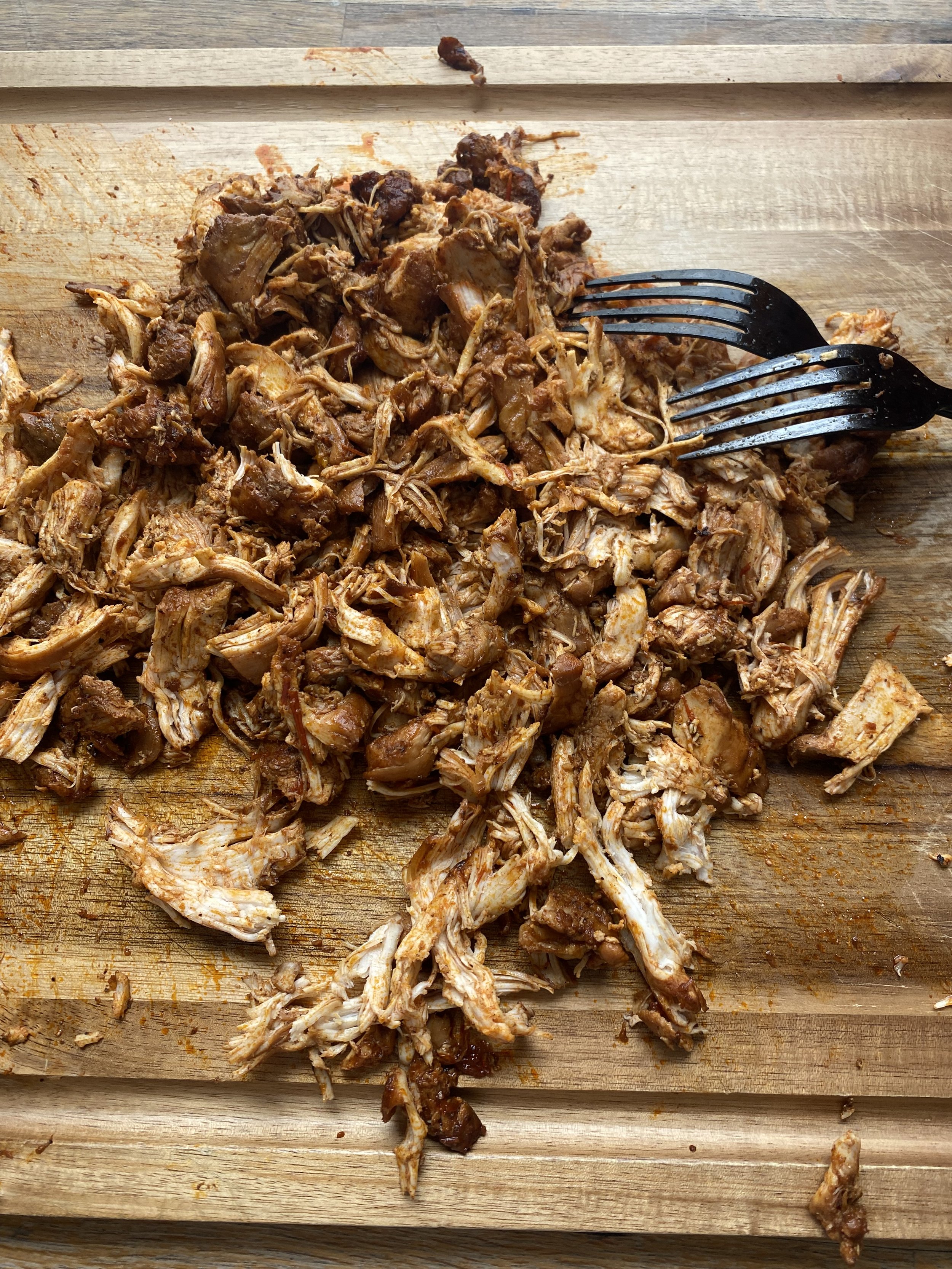 Shredded cooked chicken and meat on a wooden cutting board with a black fork.