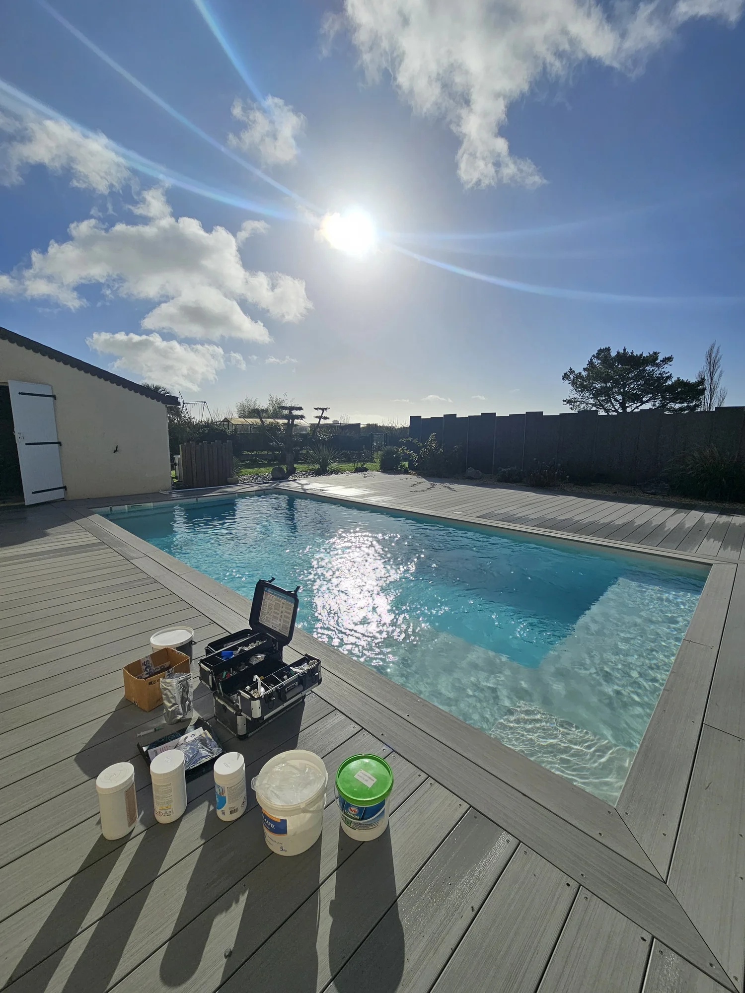 Piscine à l'eau limpide, avec la mallette d'analyse et les produits d'entretien posés sur la terrasse