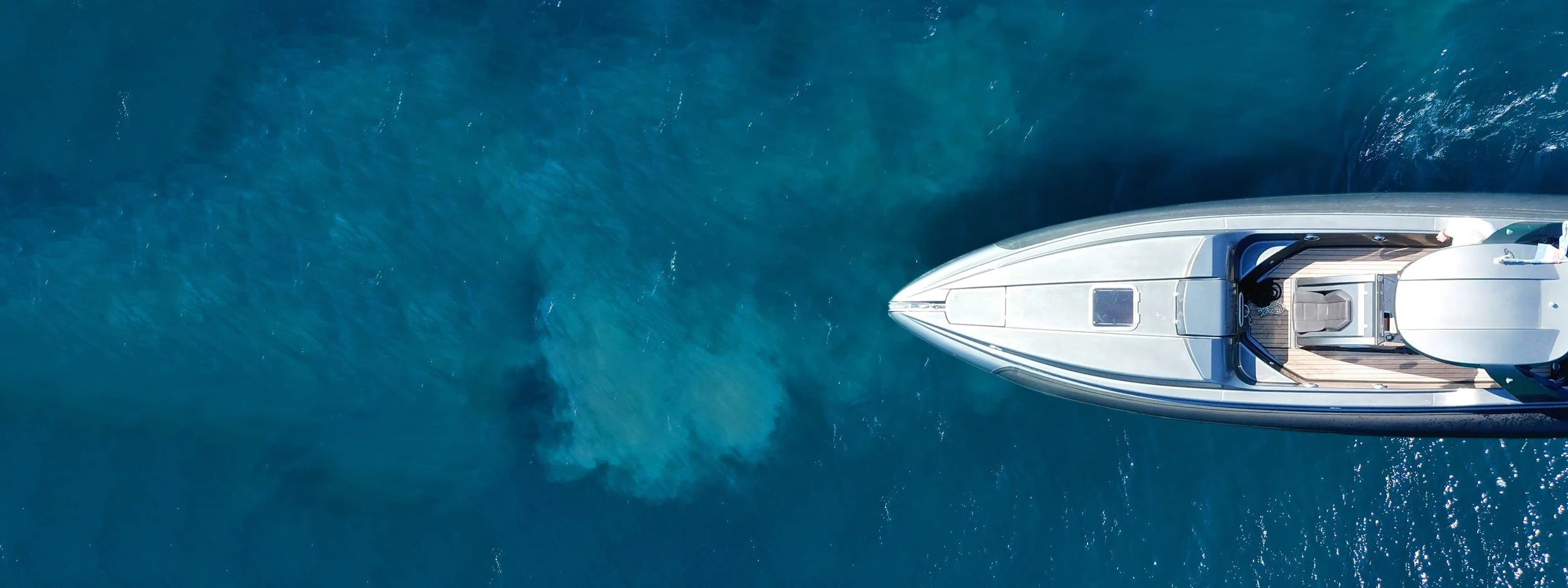 A top-view photograph of a boat out on the water. Only half of the boat is visible as it emerges from the right side of the screen.