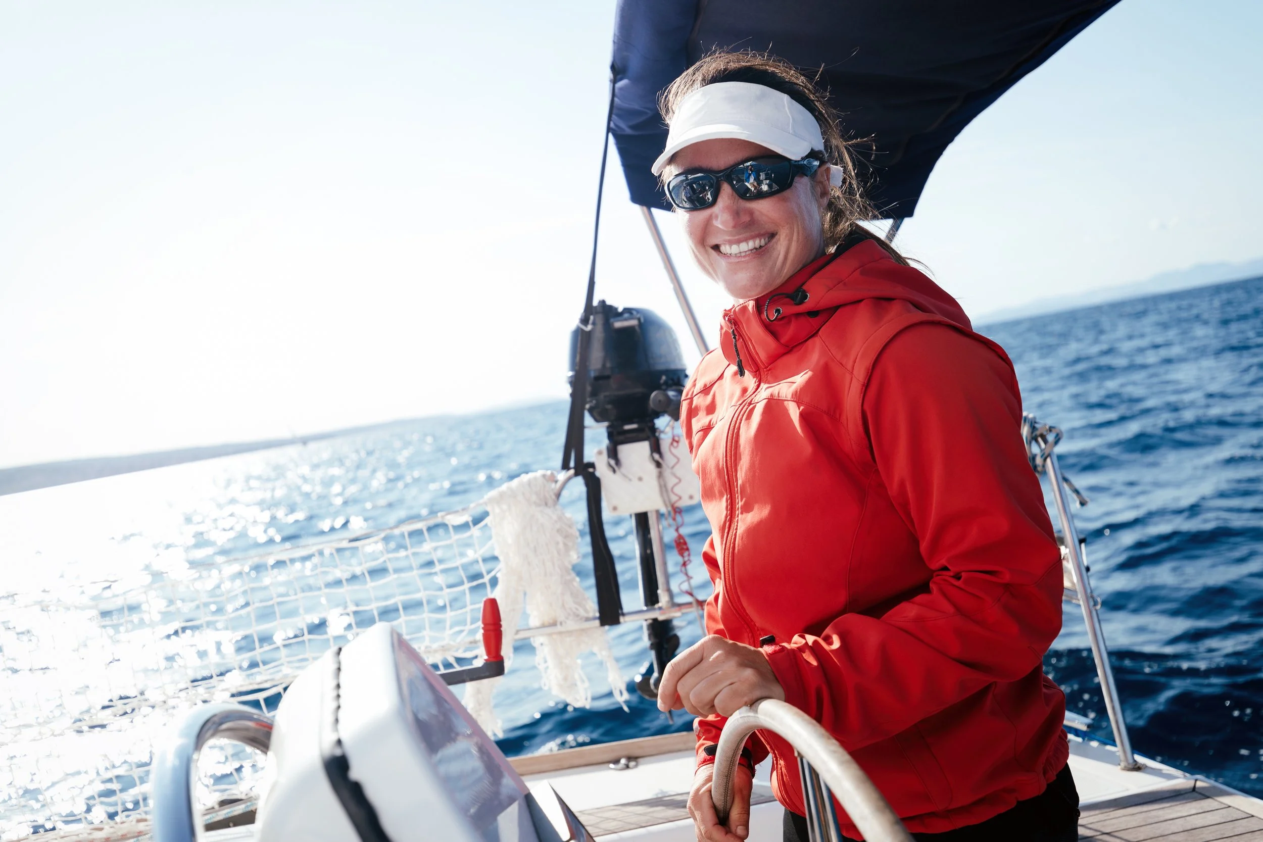 A photograph of a woman out on a boat, looking at the camera and smiling.
