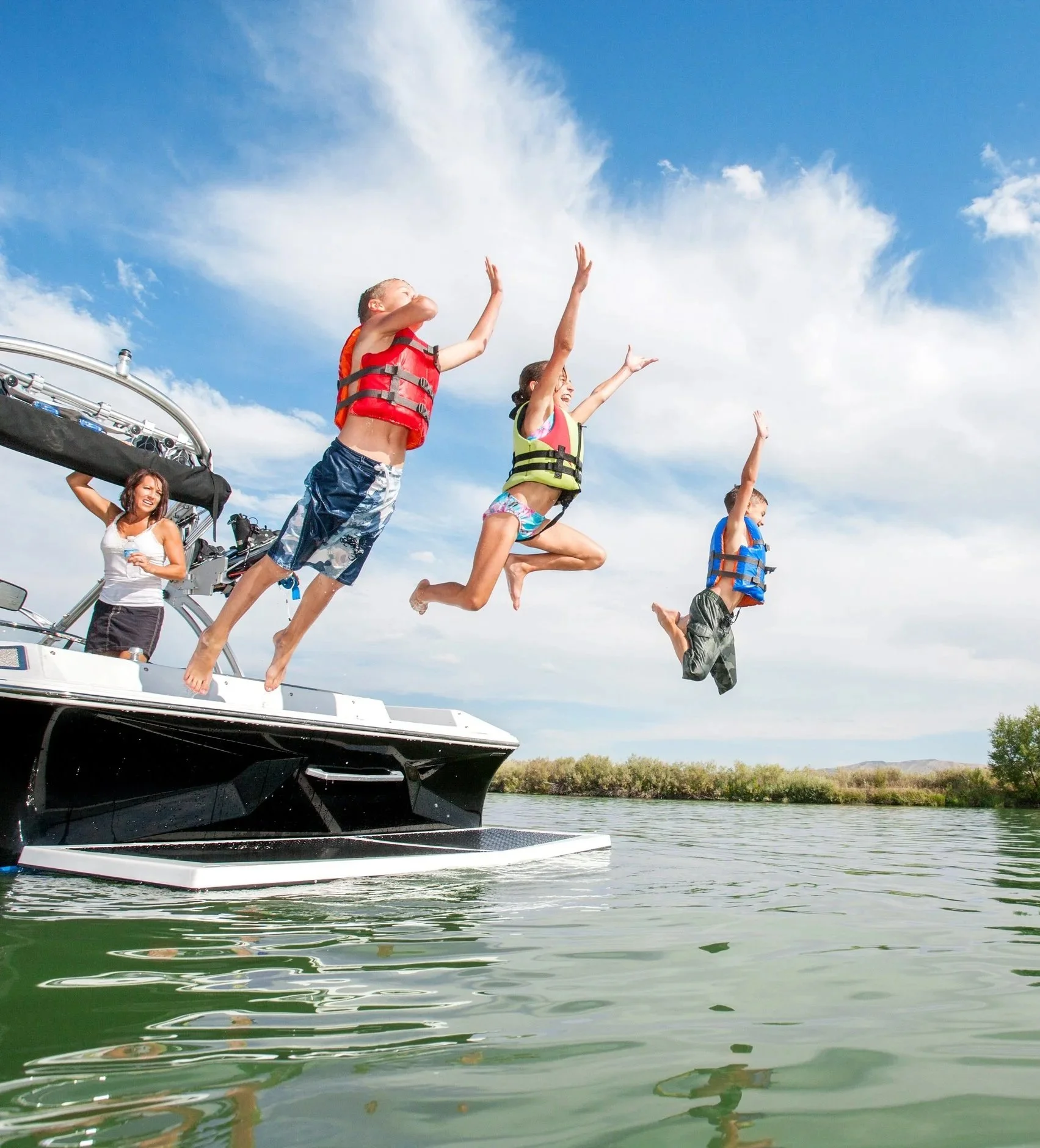 A photo of children jumping from a boat and into the water while their mother watches.