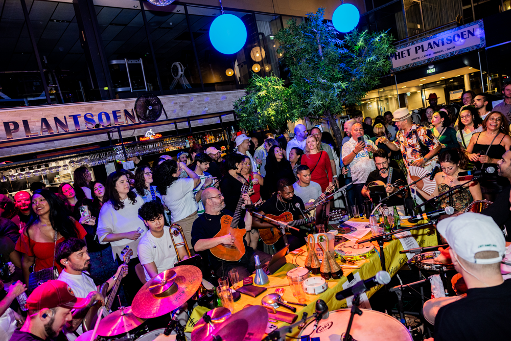 SambaRoots Feijoada & Samba at het Plantsoen musical performance with musicians playing guitars, drums, and other instruments surrounded by an enthusiastic crowd of diverse ages and backgrounds.