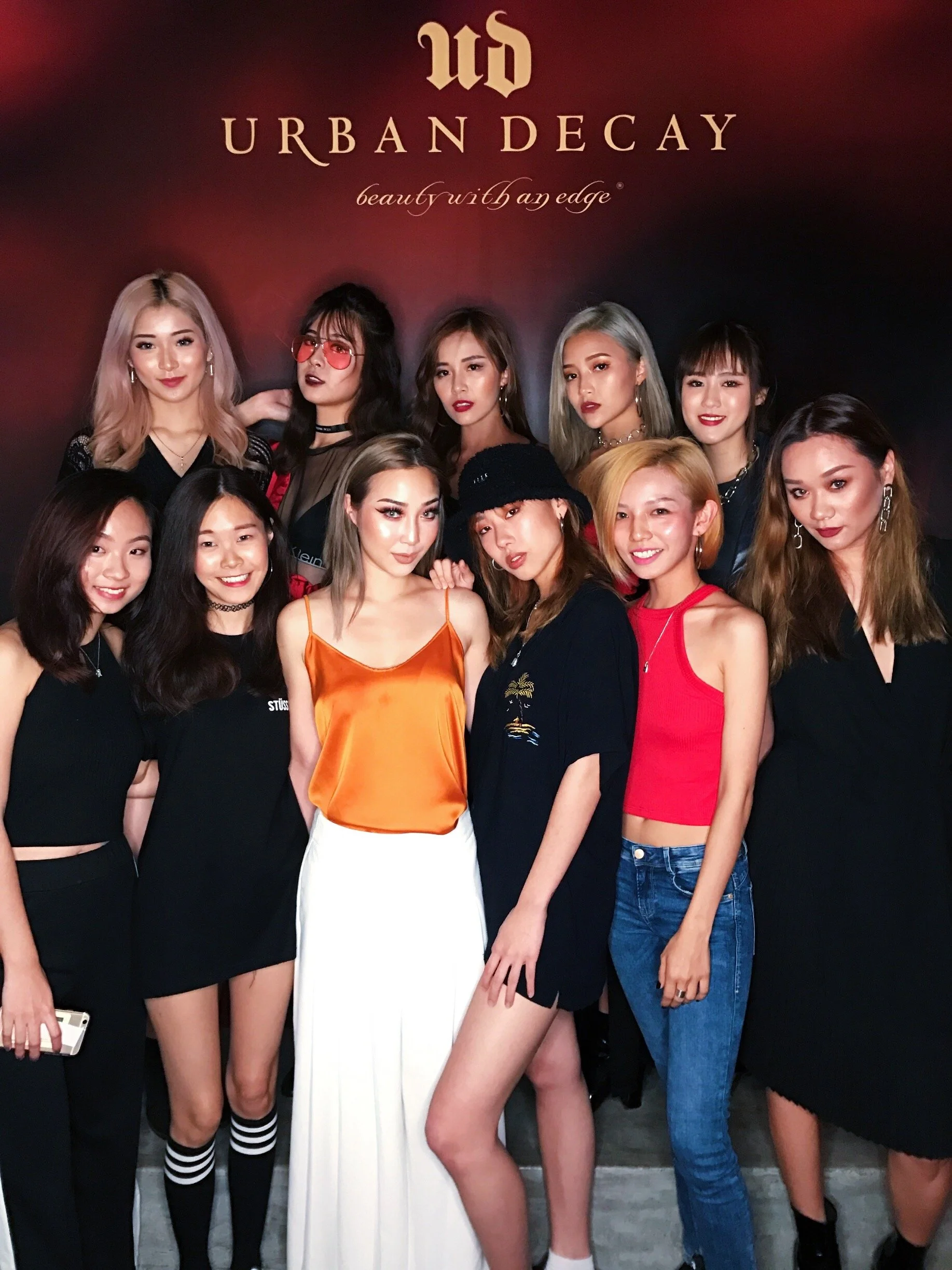 Group of ten women standing in front of a backdrop with the Urban Decay logo, posing for a photo at an event.