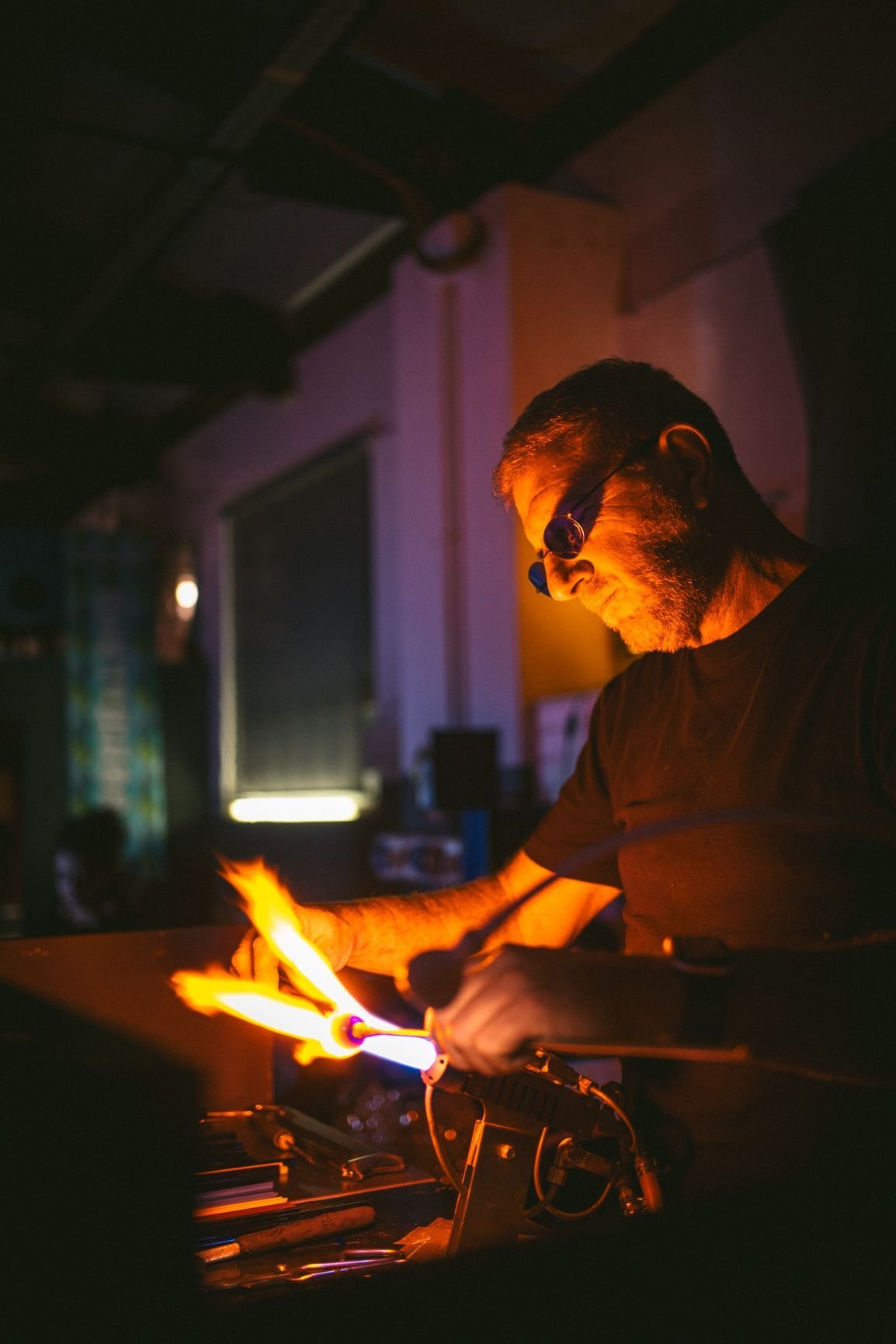 Artista. David Penso  con occhiali da riparare, che lavora con il cannello a fiamma aperta, creando un incendio visibile nel laboratorio oscuro.