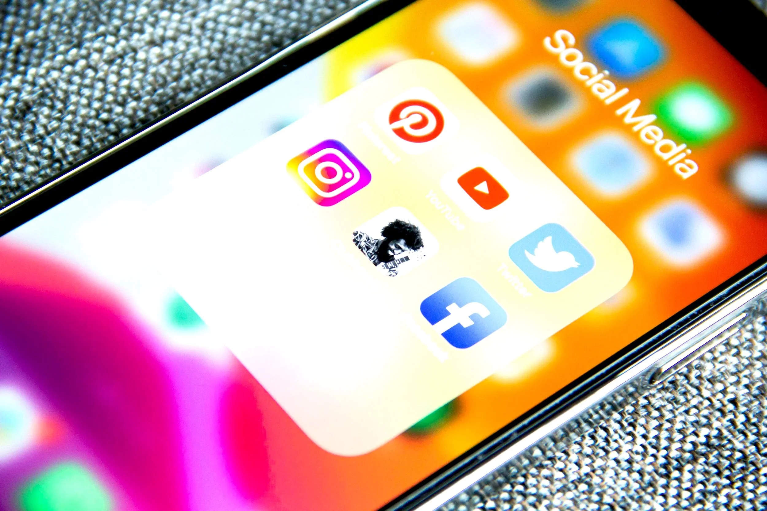 Smartphone screen displaying social media app icons, including Pinterest, Instagram, YouTube, Twitter, and Facebook, with a background of colorful blurred lights.