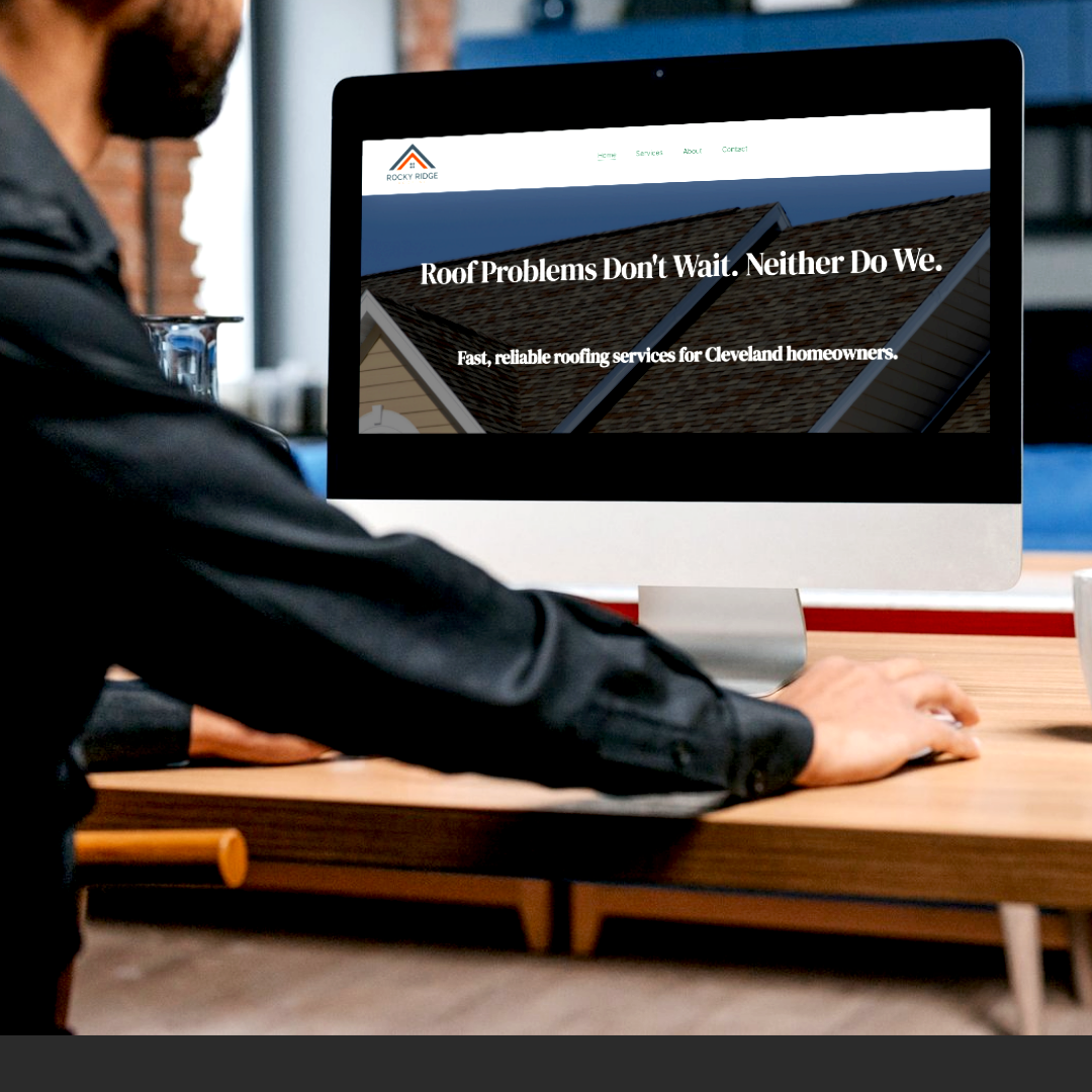 A person working at a desk looking at a desktop computer displaying a roofing company's website, Rocky Ridge, with a background image of a roof and the text 'Roof Problems Don't Wait. Neither Do We.'
