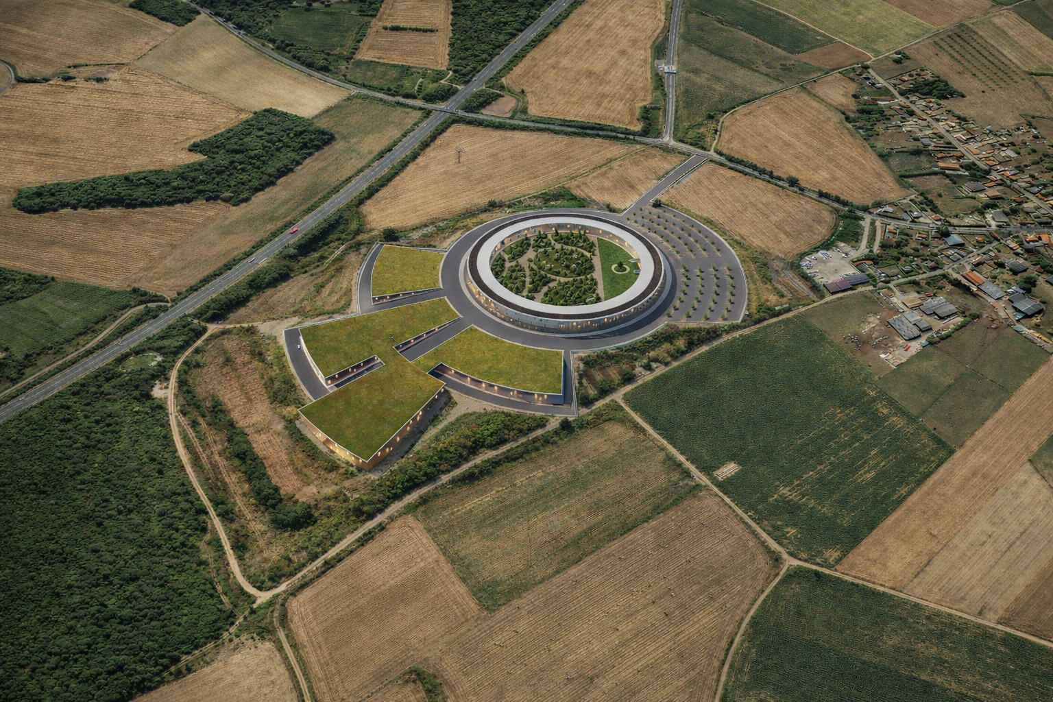 Vue aérienne d'un bâtiment moderne en forme d'anneau entouré de jardins et de parkings, situé dans une région rurale avec des champs agricoles et des zones boisées.
