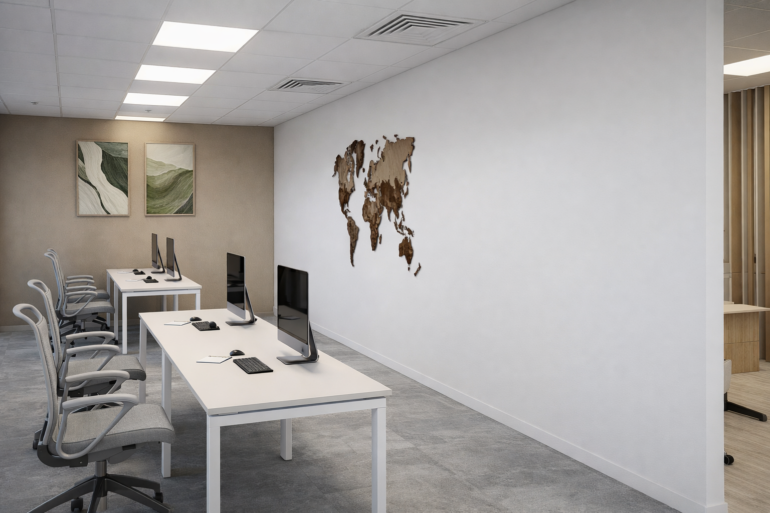 Espace de bureau avec quatre ordinateurs sur deux tables blanches, six chaises de bureau, murs décorés avec deux tableaux abstraits et une carte du monde en bois suspendue. Sol gris et plafond blanc avec éclairage intégré.