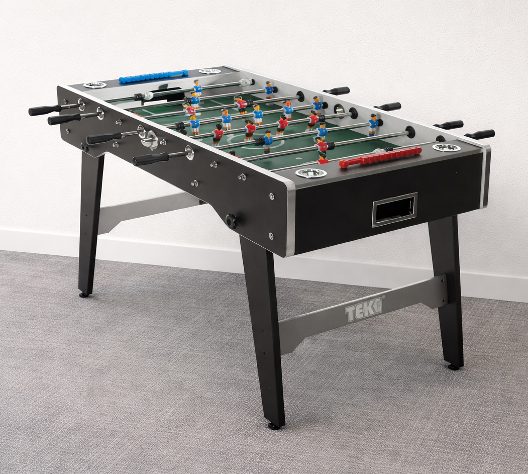 A foosball table in a room with carpeted flooring and a plain white wall.