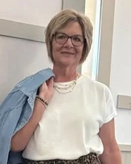 Female model wearing a white t-shirt, silver necklaces with a jean jacket thrown over her shoulder.