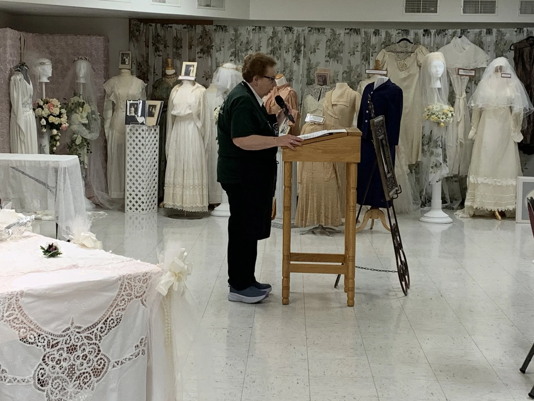 Picture of Connie speaking in front of wedding dresses at the tea