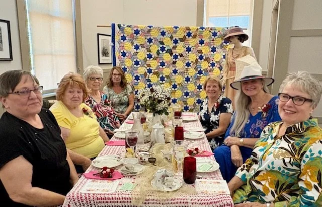 9 ladies sitting around a rectangular table decorated in red, pink and white