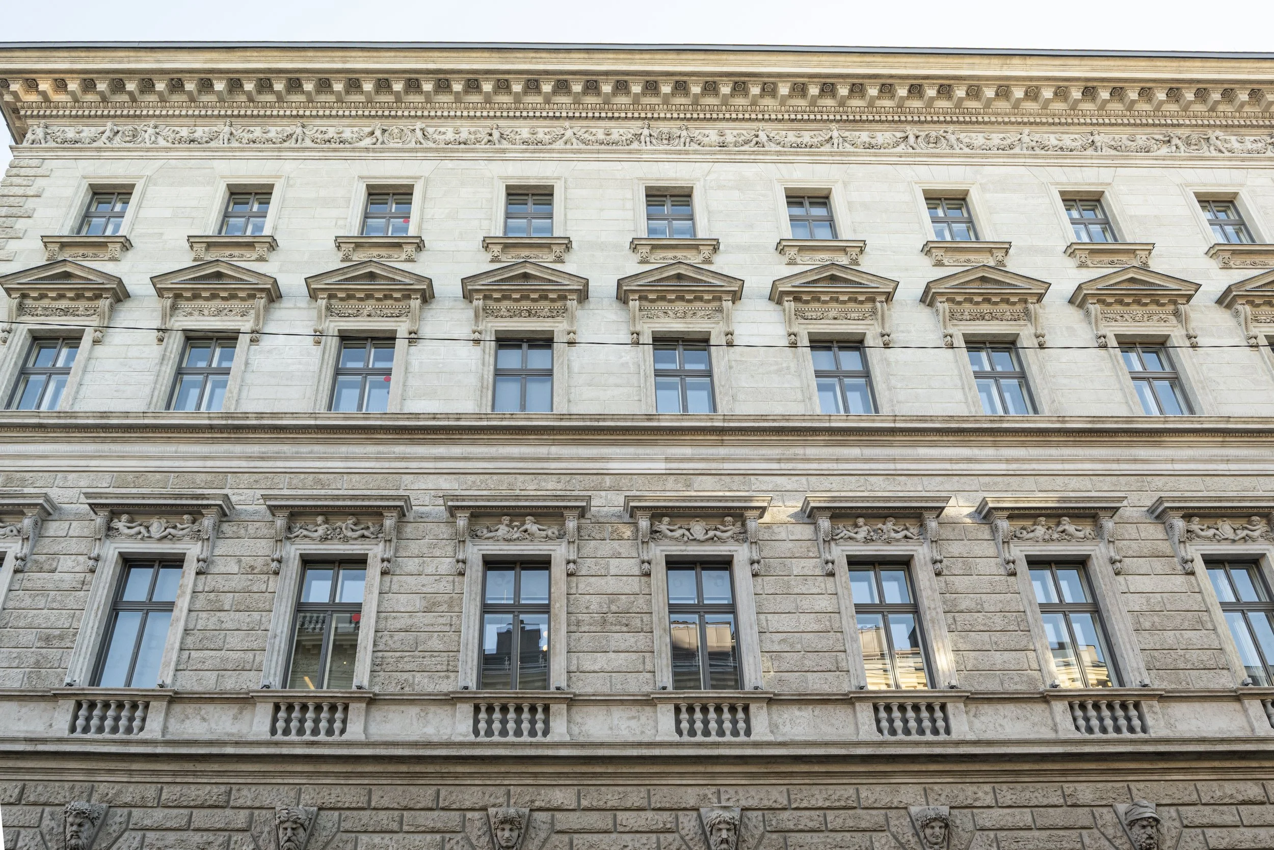 The front of a classical style building with multiple windows and ornate architectural details, including decorative sculptures and cornices.