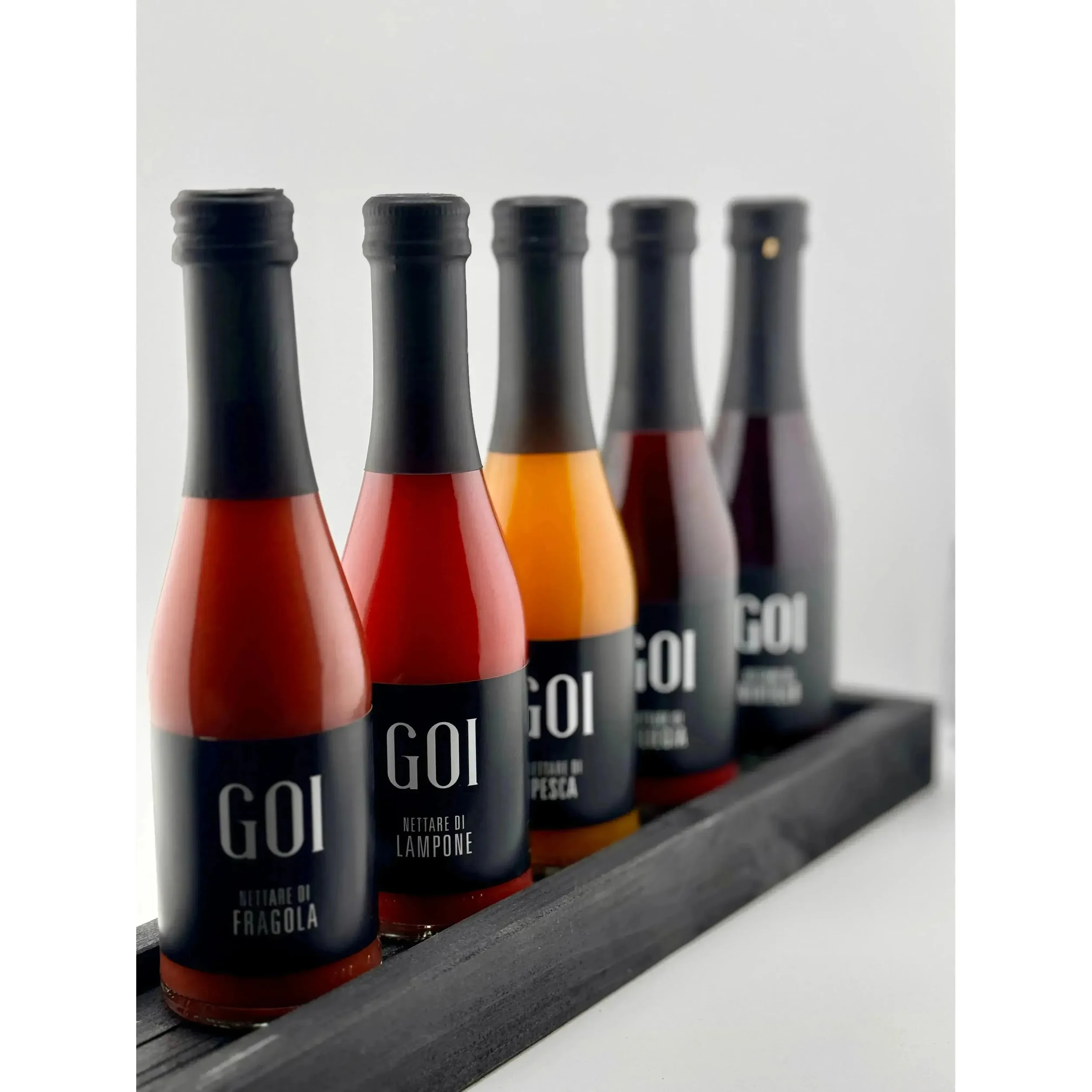 Cinque bottiglie di salsa di diversi gusti posizionate su un vassoio di legno, con etichette con scritto 'Goi'.