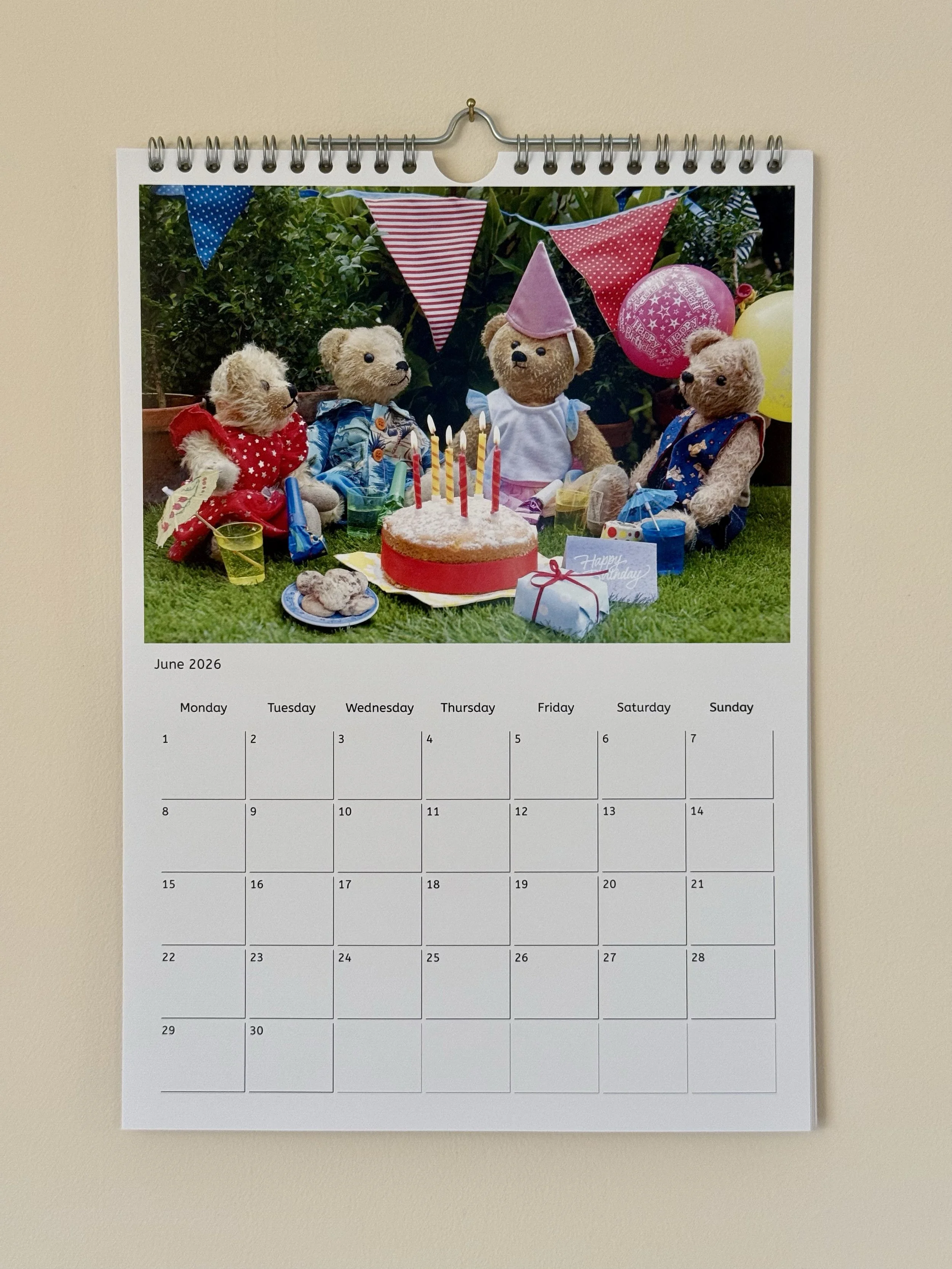 A calendar page for June 2026 with a photo of teddy bears celebrating a birthday with a cake, balloons, and party decorations.