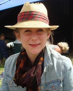 Woman wearing a straw hat with a red plaid band, denim jacket, and a patterned scarf, outdoors