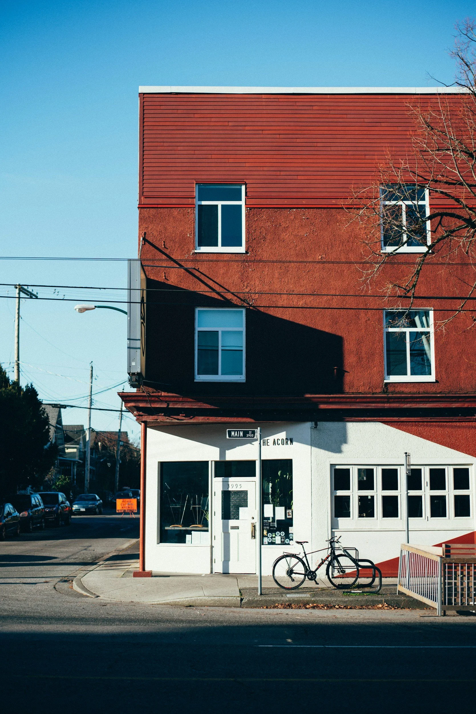 Red building with white storefront on street corner, bicycle locked to bike rack in front, and a street sign reading 'Main'