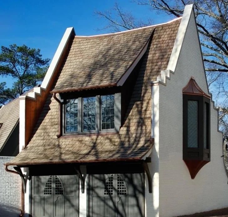 A house with a steep, gabled roof, white brick walls, and distinctive curved window bays, resembling the style of a fairytale cottage.