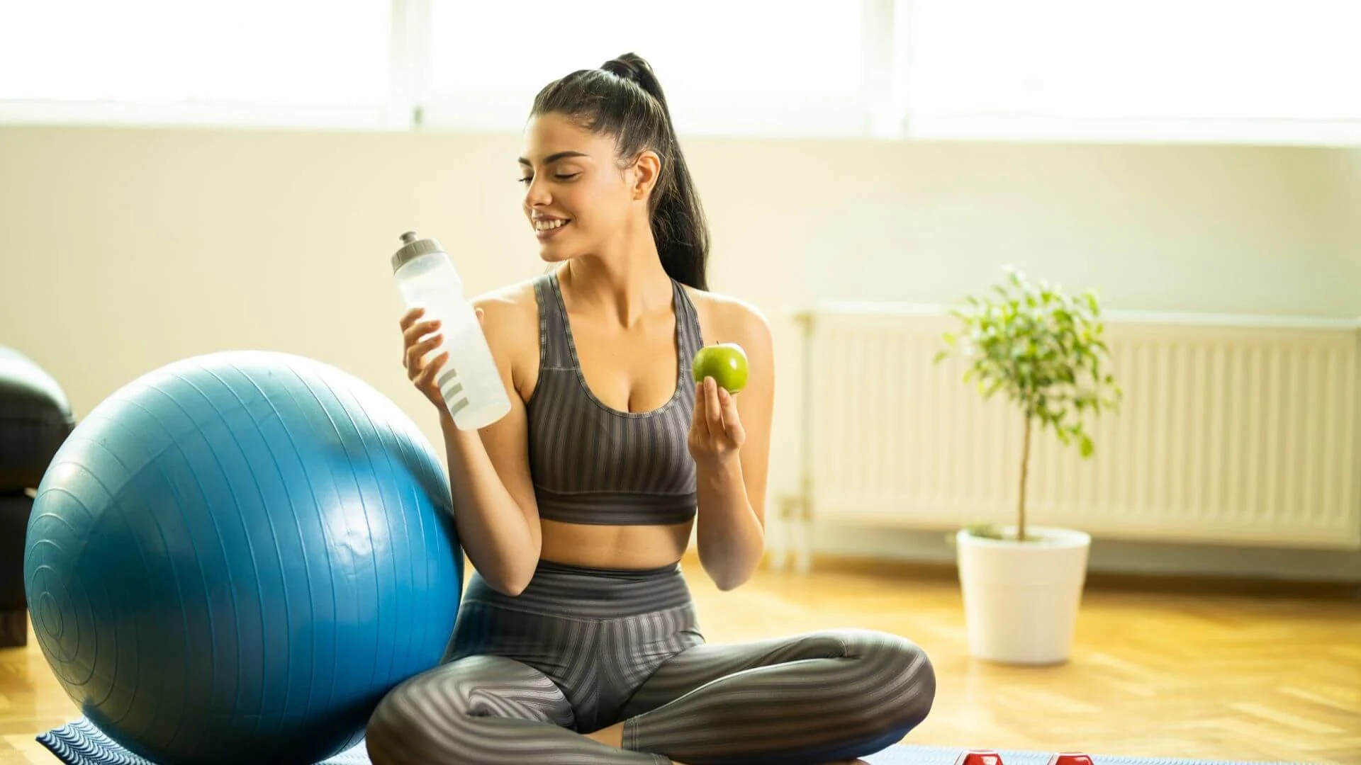 woman smiling while looking at her healthy water with an exercise ball next to her