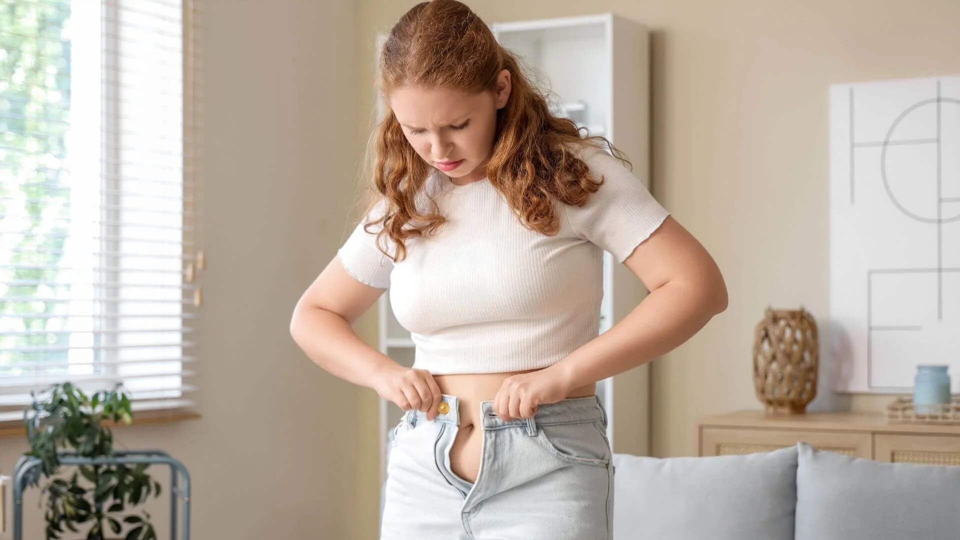 woman looking upset she can't get her jeans to button up