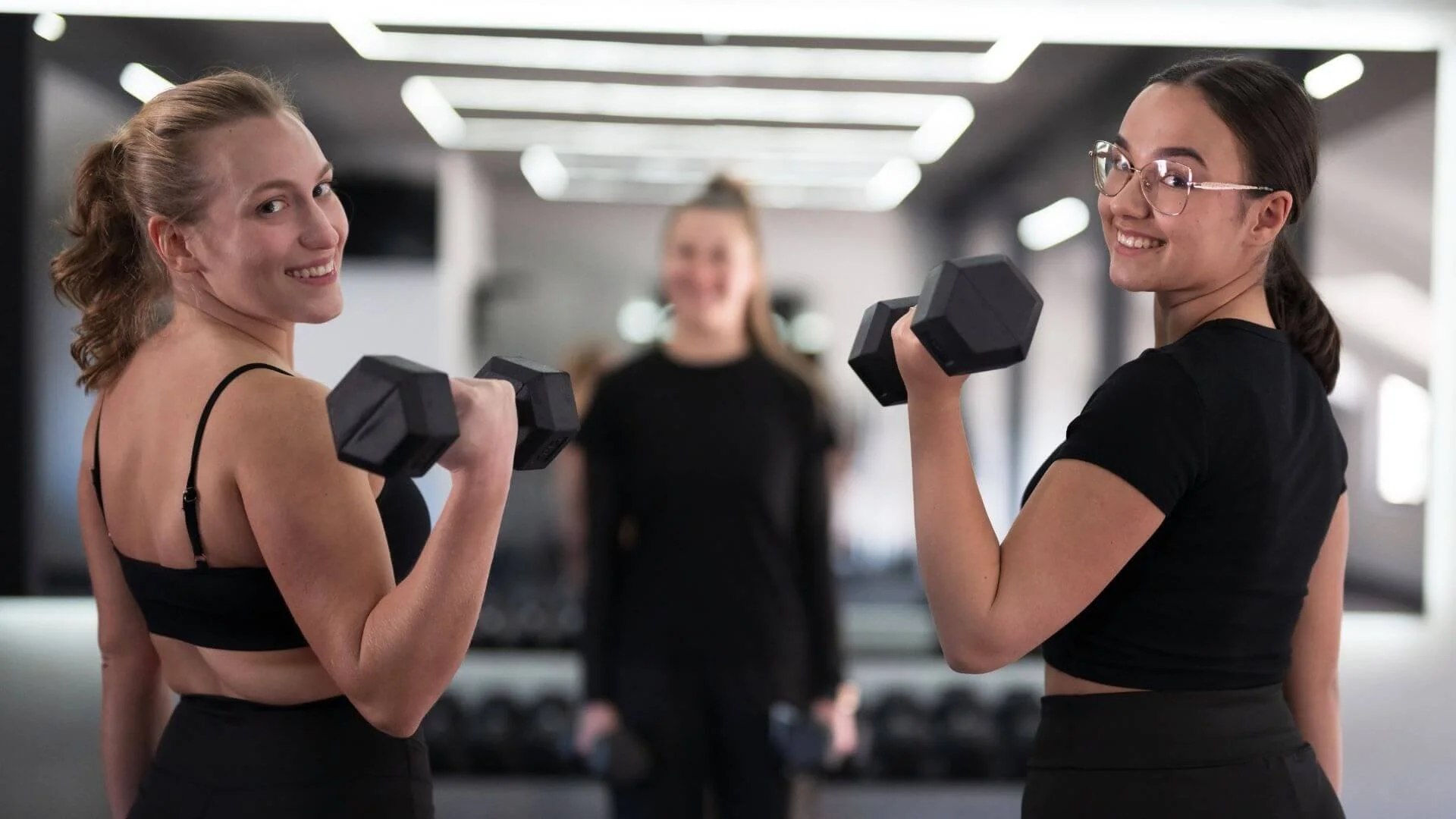 two women happily engaging in weight training with a female personal trainer