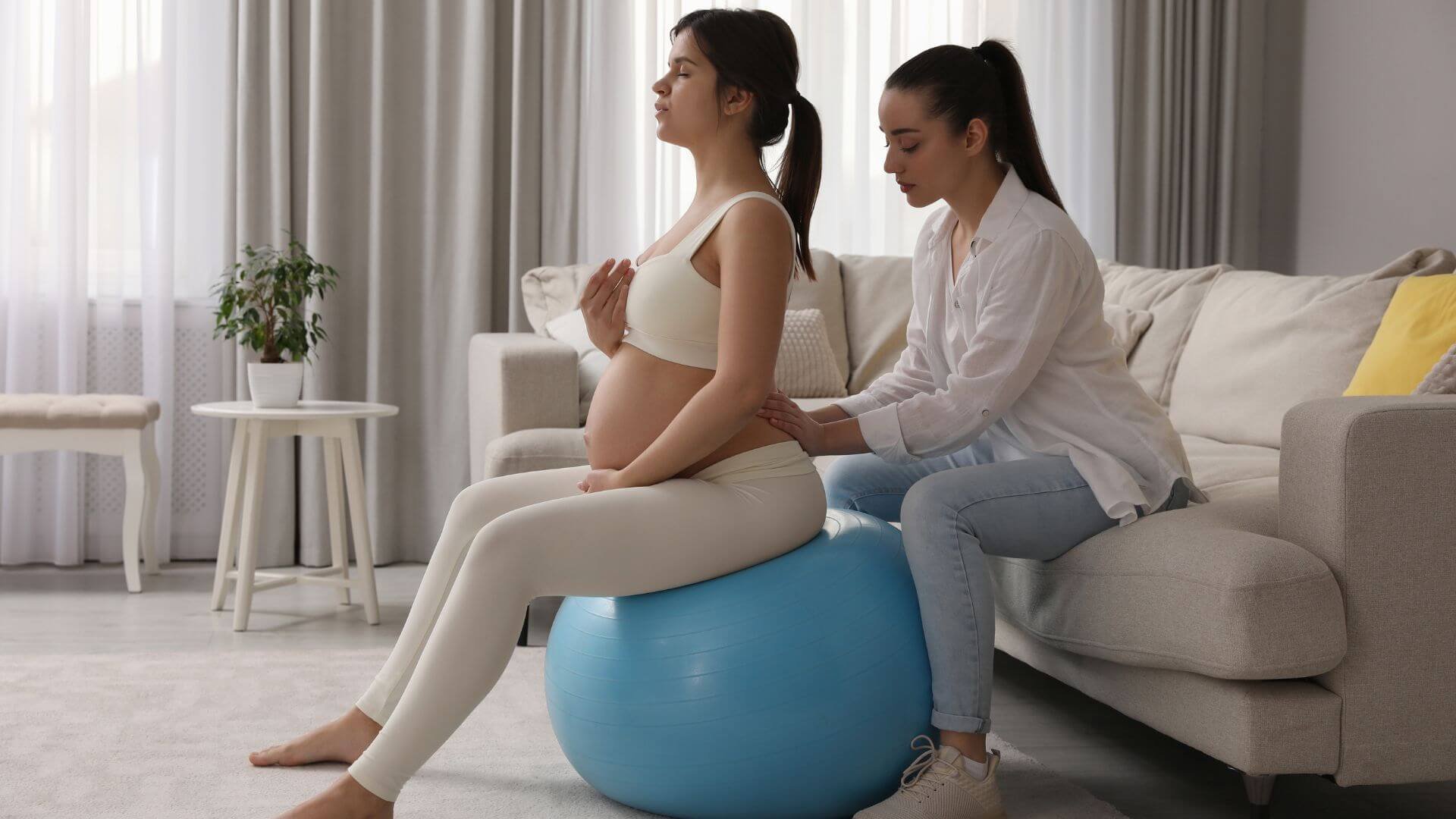 pregnant woman getting support while doing ball exercises