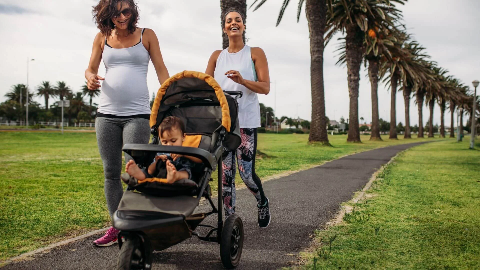two women, one pregnant and one pushing her baby in a stroller,  happily walking together