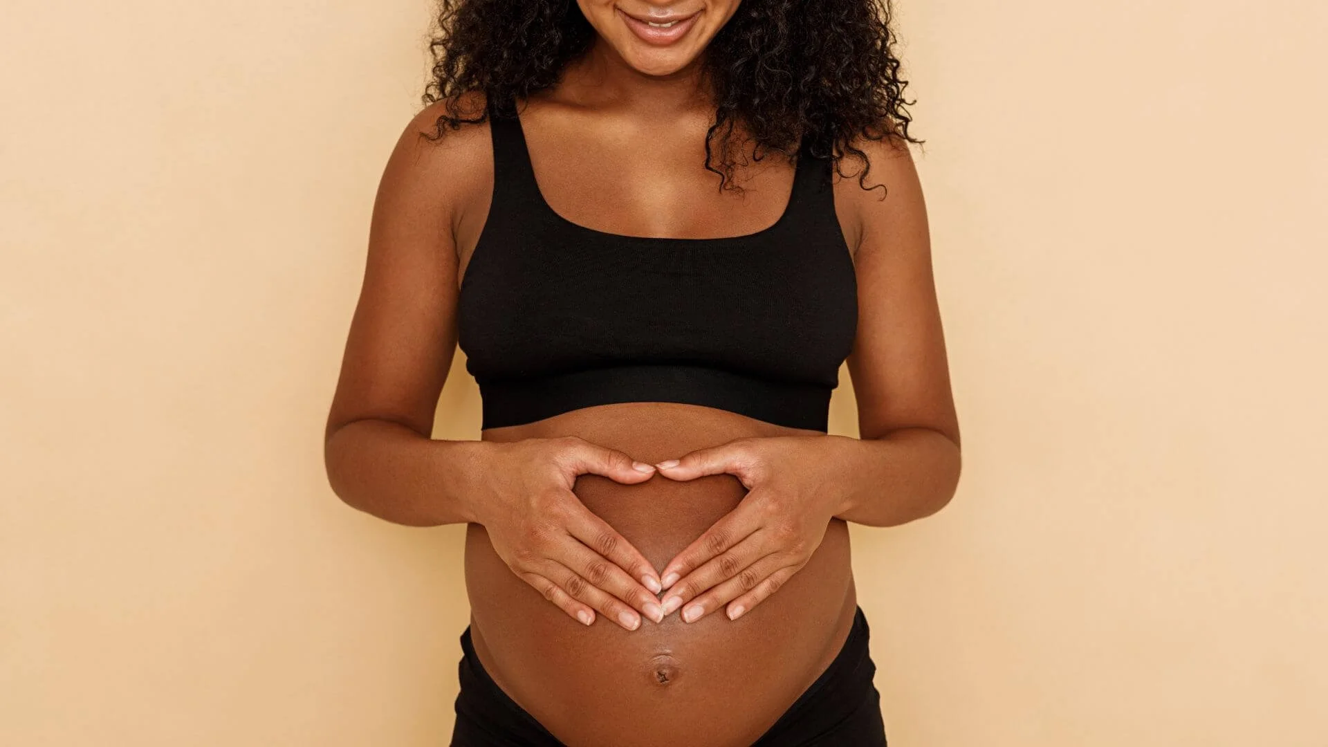woman making a heart with her hands over her pregnant belly