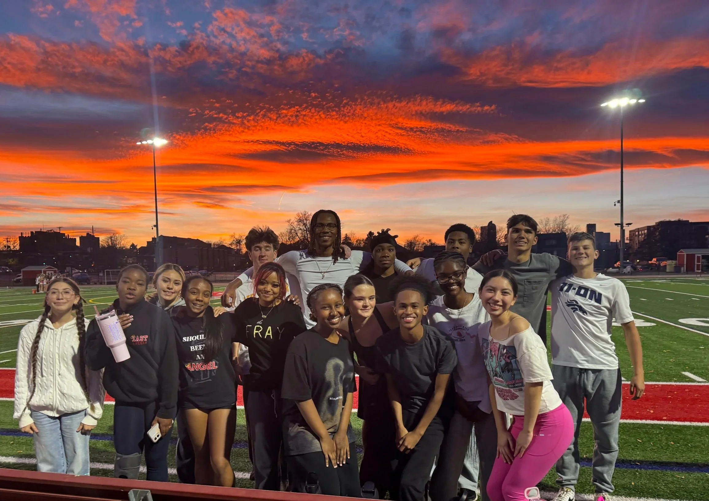Group of diverse young people posing for a photo on a sports field at sunset.