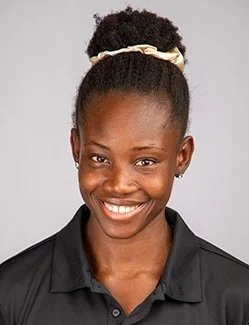Portrait of a smiling woman with natural hair styled in a puff, wearing a black collared shirt, and a light-colored headband.