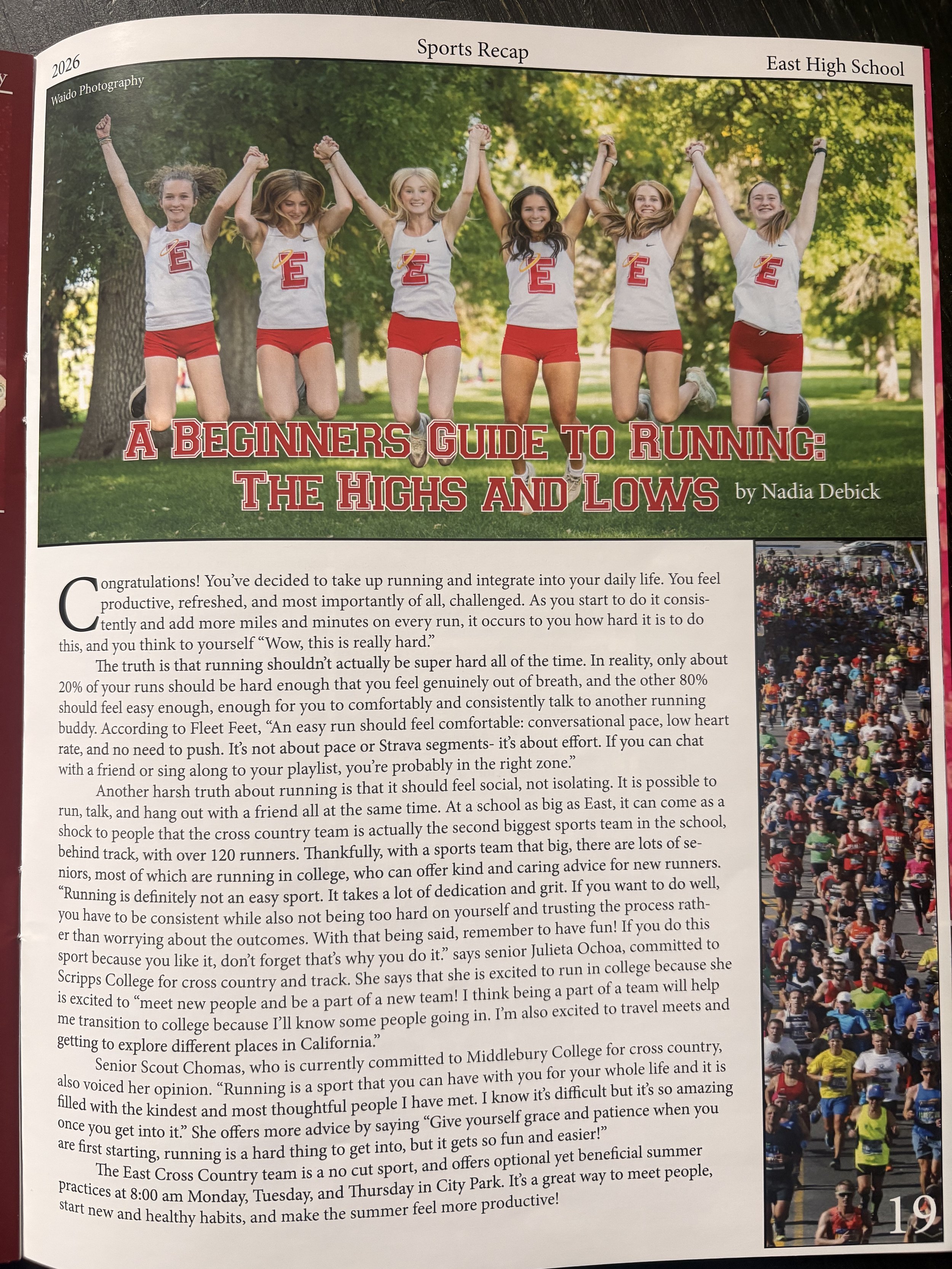 A page from a magazine features a photograph of six young women in athletic running uniforms jumping in the air outdoors with trees and sunlight in the background. The page title is 'Sports Recap' from East High School, and the headline reads 'A Beginners Guide to Running: The Highs and Lows' by Nadia Debick. The right side of the page contains a large photo of a crowd of runners participating in a race on a sunny day.