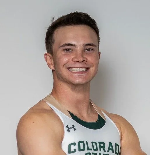 A young man smiling, wearing a white athletic jersey with green accents, and the words 'Colorado' on it, standing against a plain light-colored background.