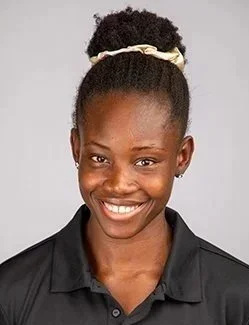 Portrait of a woman smiling, wearing a black collared shirt and a white headband, with her hair in a puff.