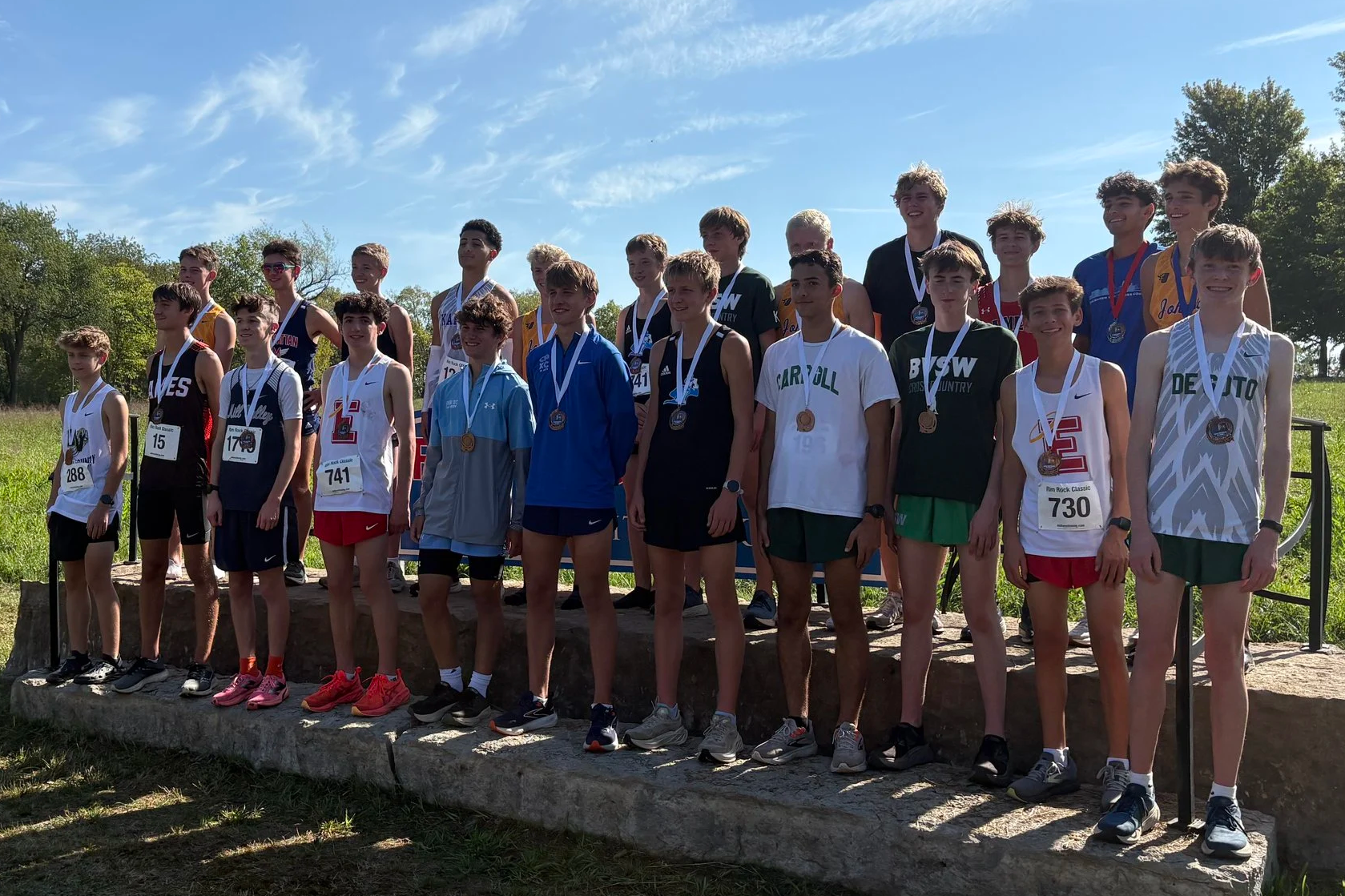 Group of teenage runners standing on podium with medals after a race, outdoors on a sunny day.