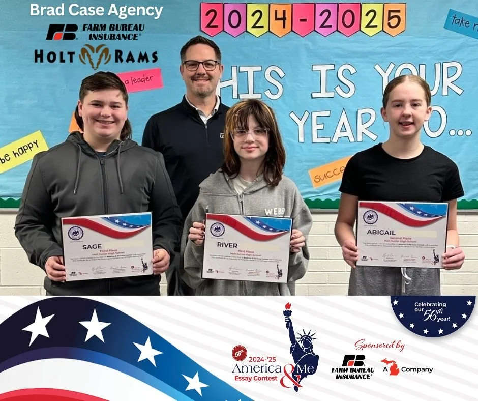 Three students and a man standing in front of a blue bulletin board holding certificates for winning a patriotic essay contest. The bulletin board has colorful cutouts of the year 2024-2025 and phrases like "His is your year" and "be happy." The students are named Sage, River, and Abigail, holding their awards for third, first, and second place, respectively.