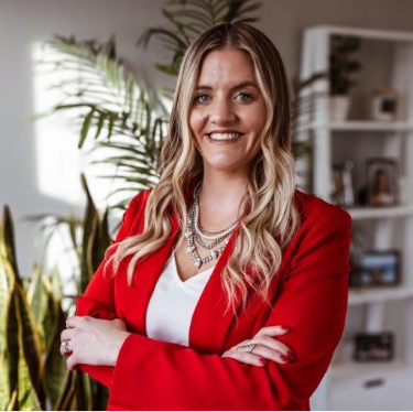 Professional headshot of a man with glasses, wearing a blue suit, white shirt, and red tie, smiling against a dark background.